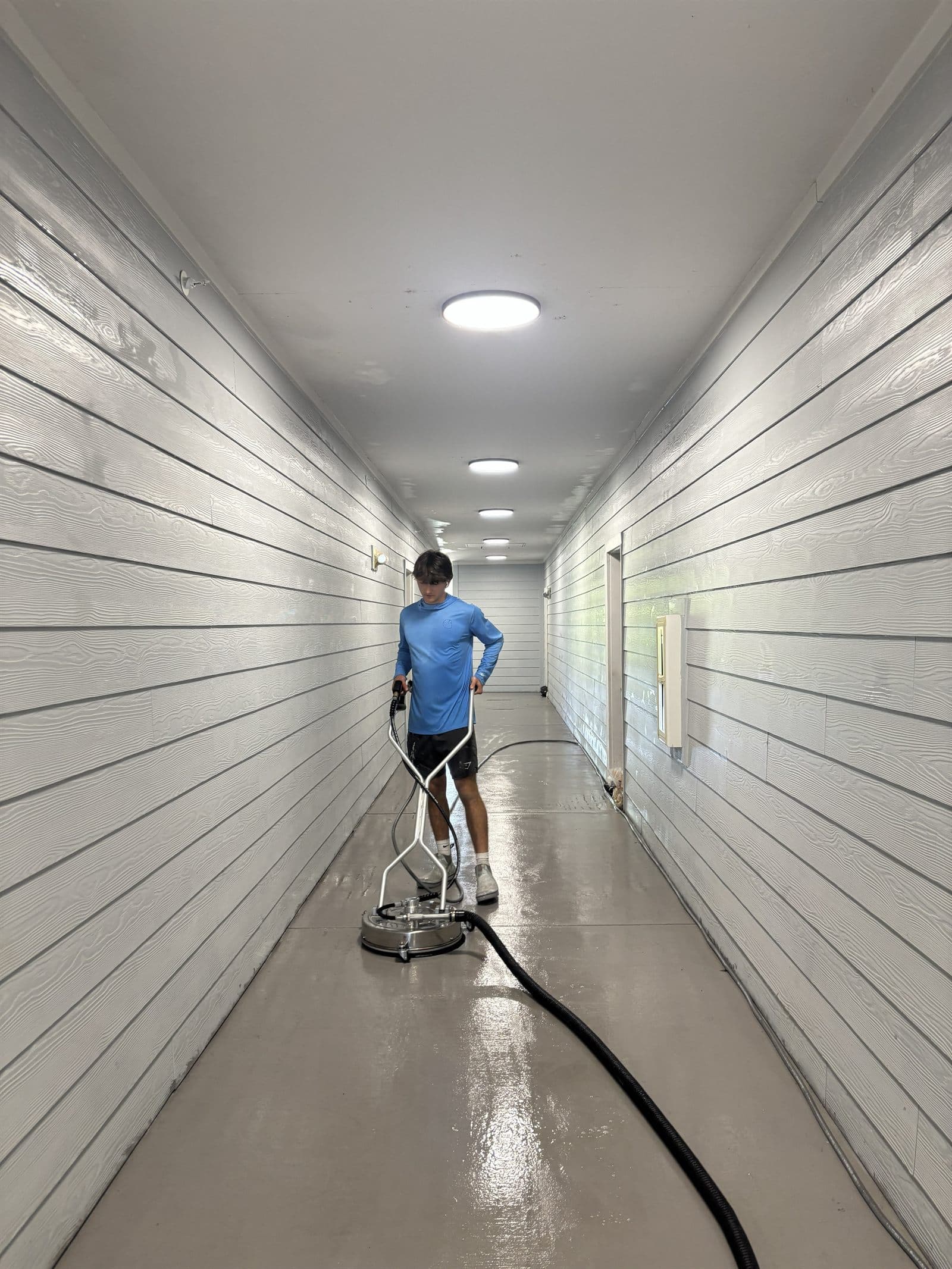 Hyphen Brothers crew member pressure washing a concrete breezeway with a surface cleaner